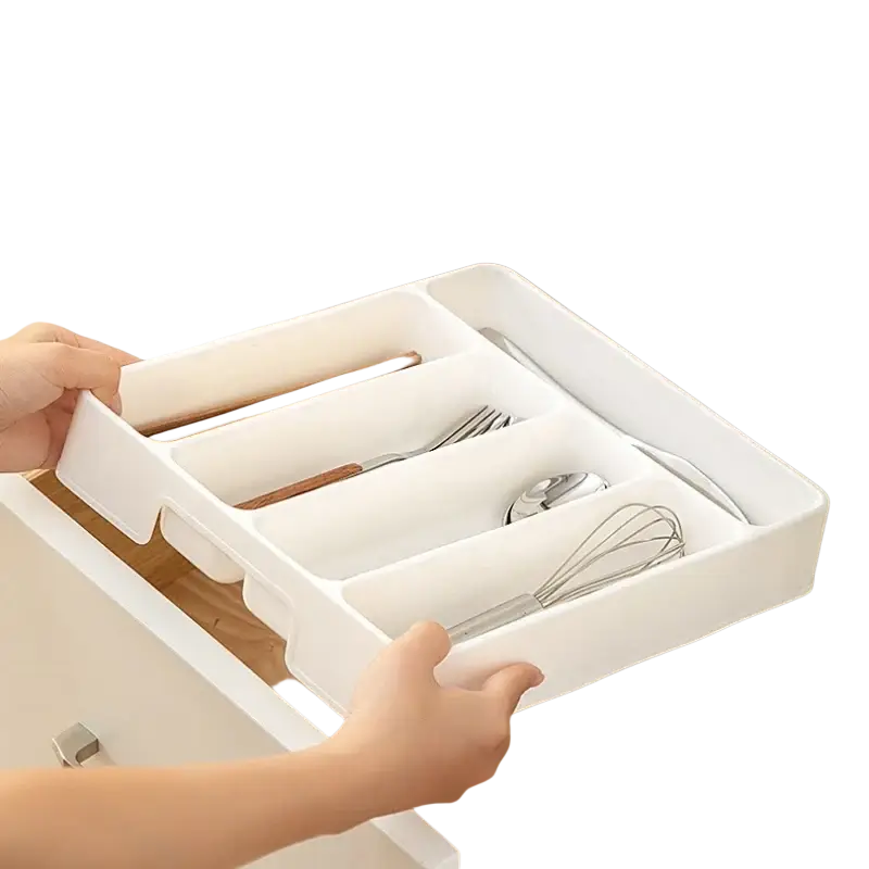 White plastic adjustable kitchen drawer utensil organizer tray with segmented compartments holding utensils and a whisk