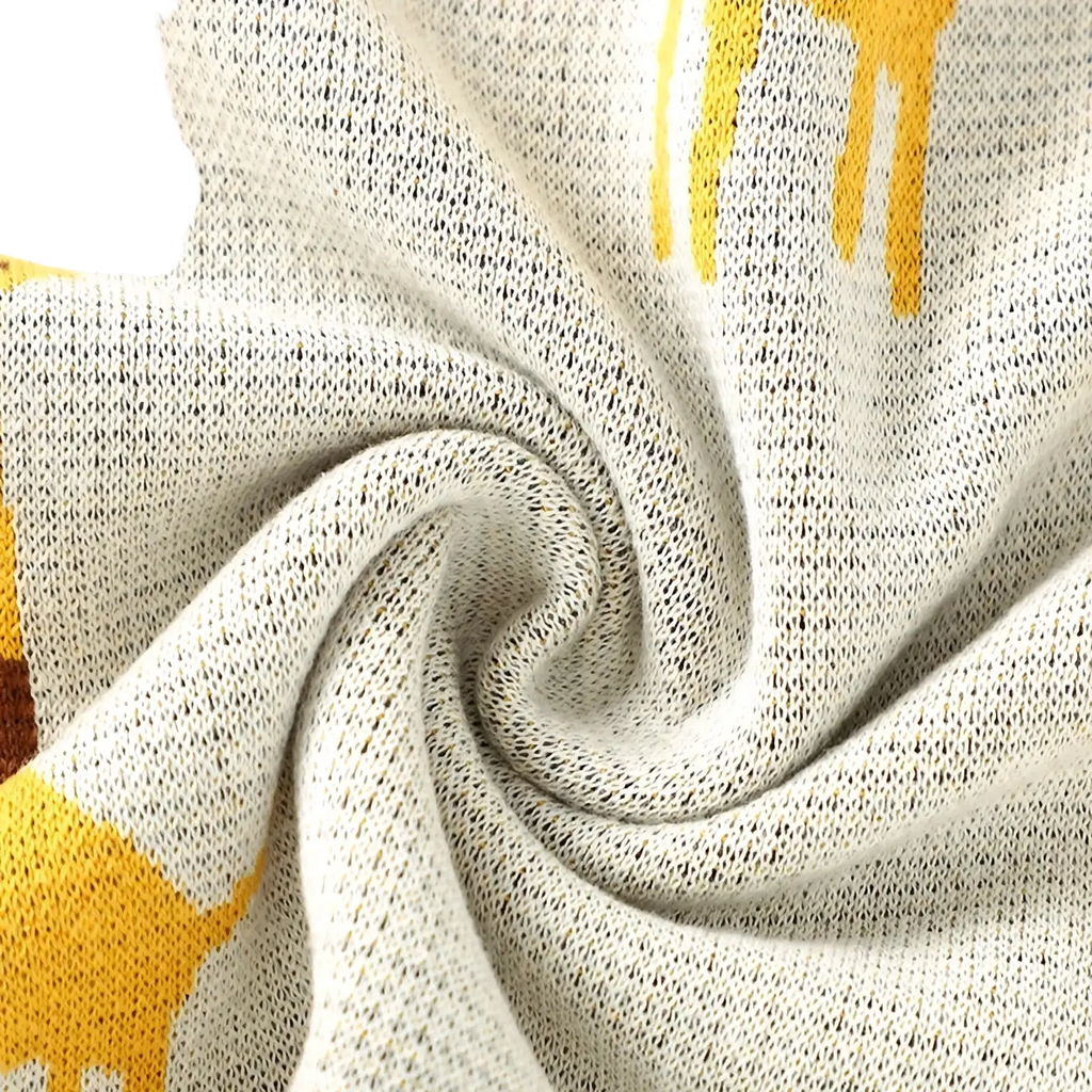 Knitted cotton giraffe baby blanket in off-white with a soft texture and playful yellow giraffe pattern