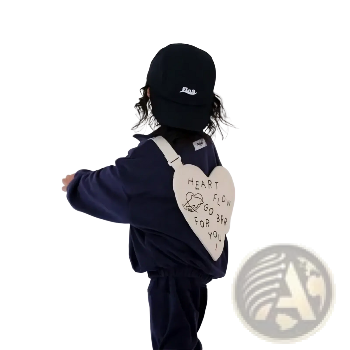 A cream-colored heart-shaped Korean kids crossbody bag with black embroidery worn by a child in navy blue clothing