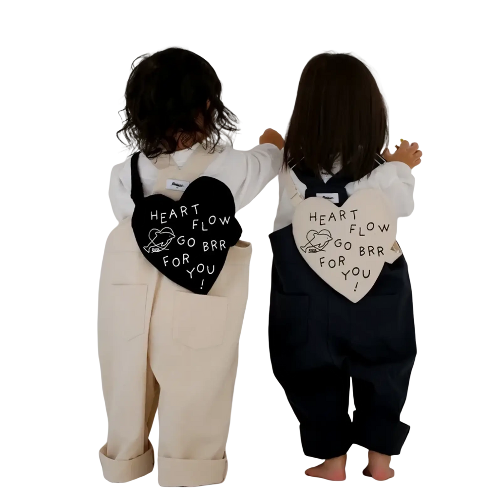 Back view of two children wearing black and white Korean kids heart crossbody bags with heart-shaped patches and playful text