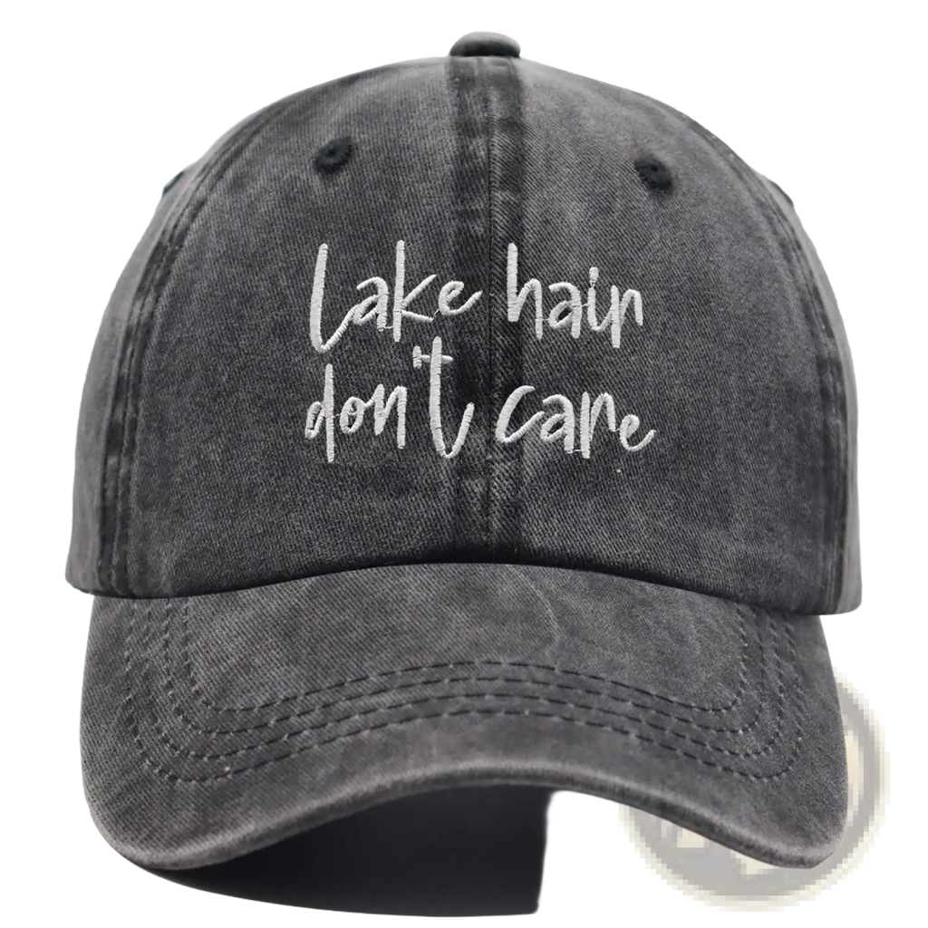 A faded gray denim baseball cap with white cursive embroidery lake hair dont care from the lake hair distressed baseball cap set