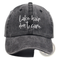 A faded gray denim baseball cap with white cursive embroidery lake hair dont care from the lake hair distressed baseball cap set