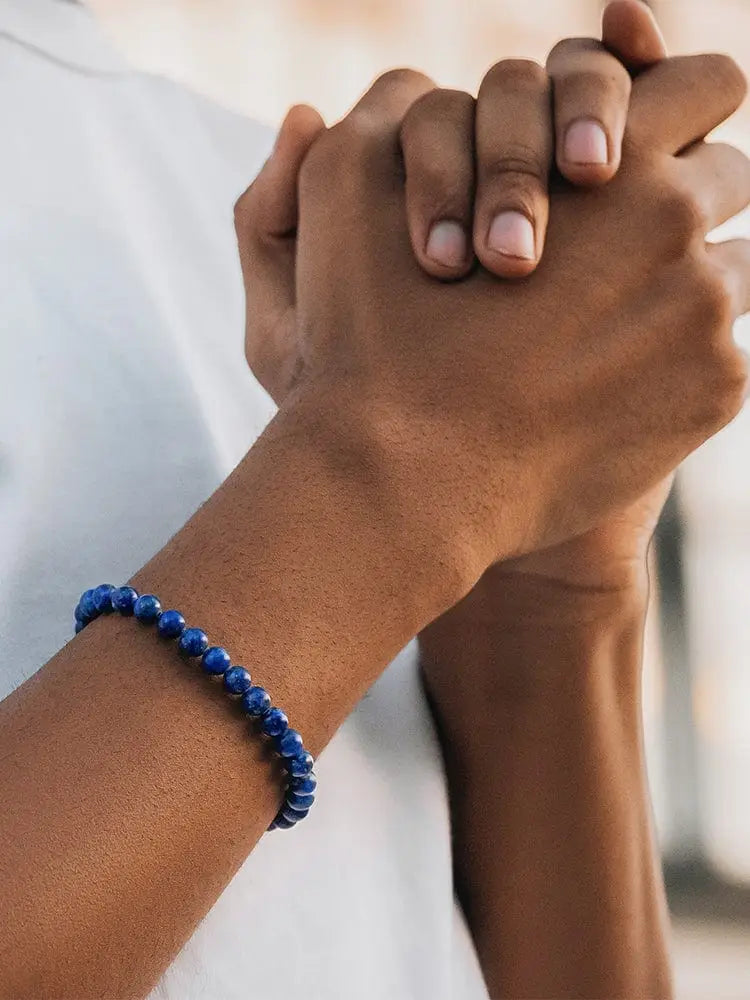 A vibrant blue AAA lapis lazuli beaded bracelet with a smooth polished finish and silver Greek key chain adorns the wrist