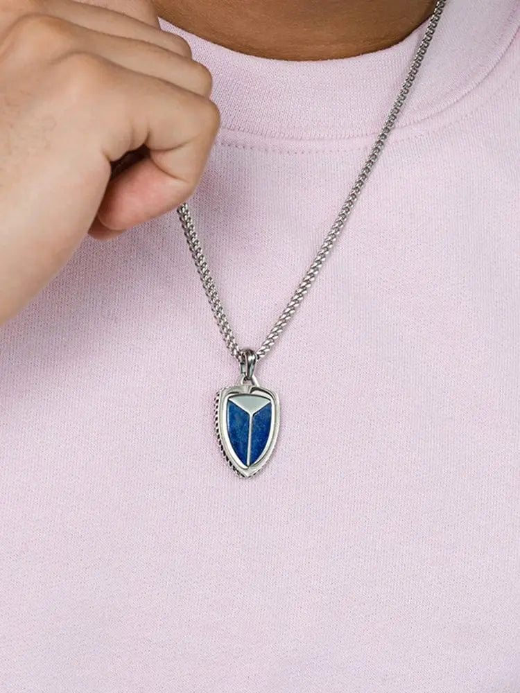 Silver shield-shaped lapis lazuli pendant with blue inlay and textured edges on a 316l stainless steel chain