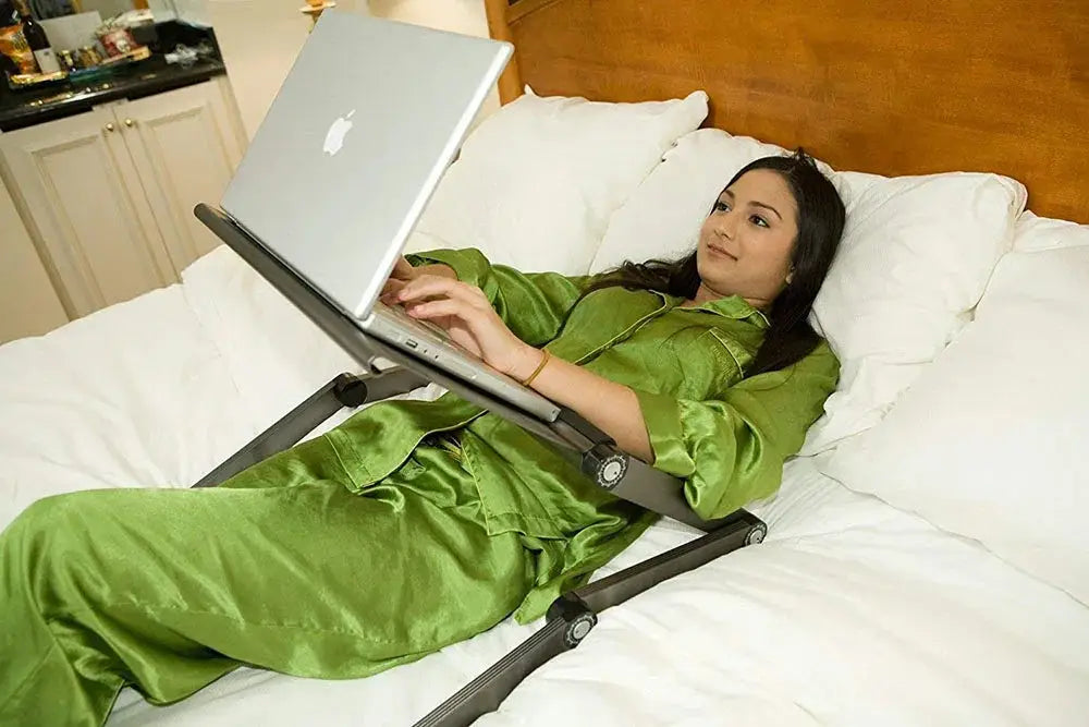 Silver laptop resting on a black ergonomic folding laptop desk with cooling fan and built-in mouse pad