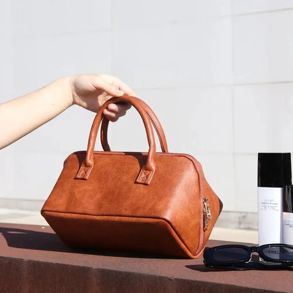 A large tan pu leather travel makeup and toiletry organizer with rounded top handles and gold-tone zipper