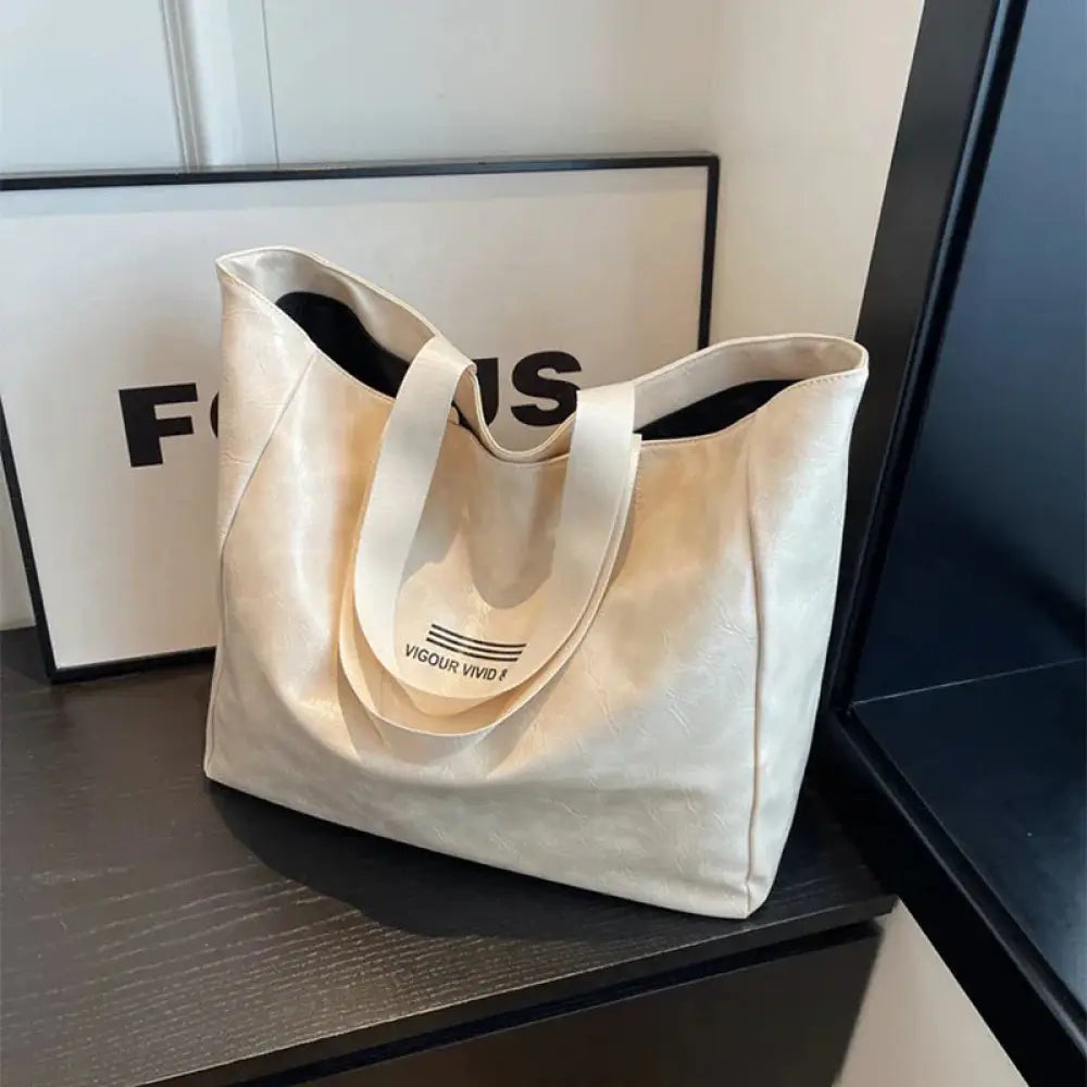Cream-colored large waterproof glossy canvas tote bag with black interior and minimalist vigour vivid branding on handle