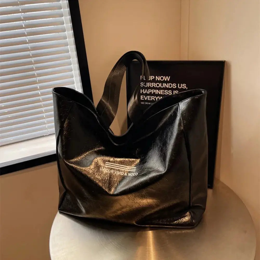 Black faux leather large waterproof glossy shoulder tote bag with gold foil logo patch and text on the front side