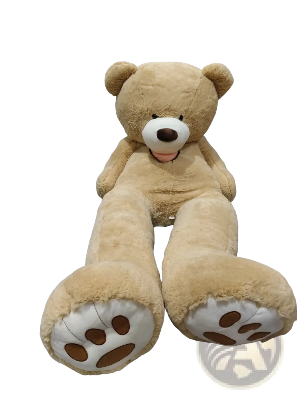 A large plush teddy bear soft velvet toy in tan with white snout and brown nose sitting upright on plastic sheeting