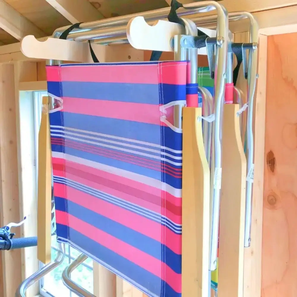A vibrant pink and blue striped fabric beach chair with wooden legs hanging on stud mounted steel lawn chair storage hooks