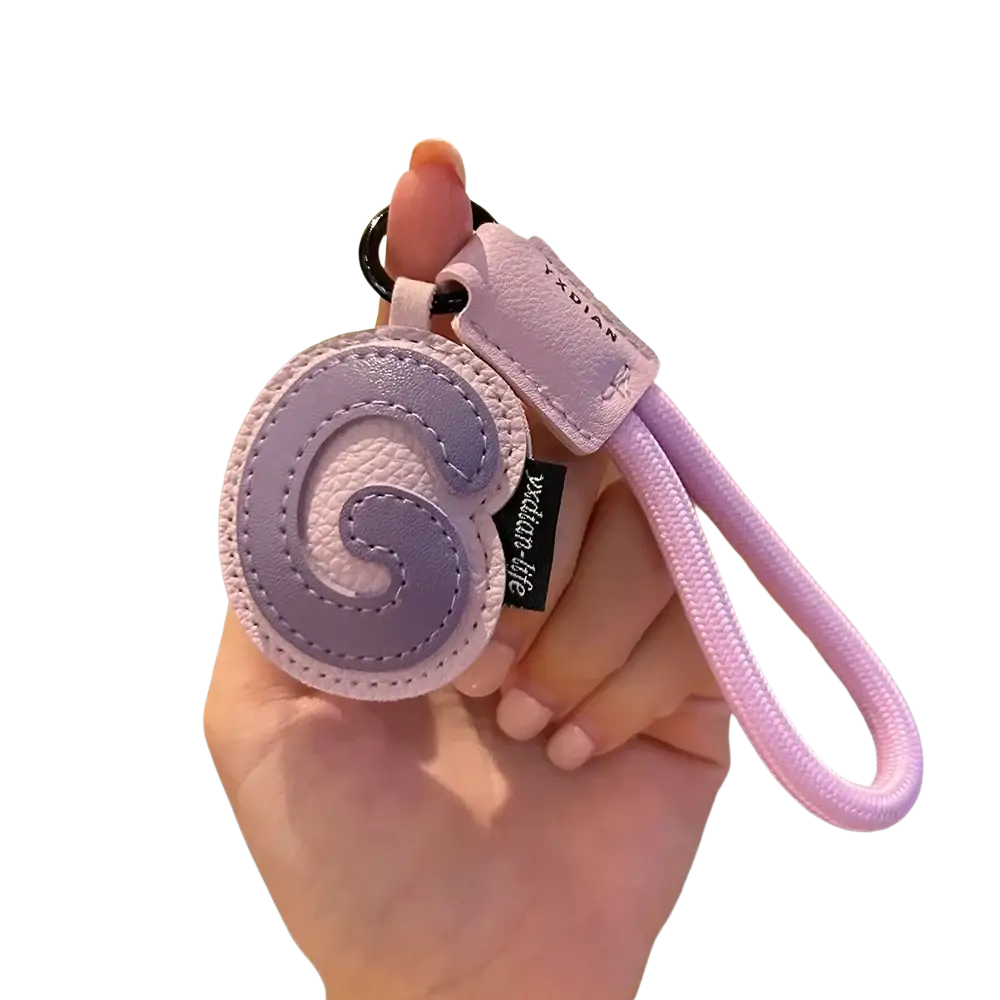 Lavender leather initial keychain with stitched letter g design, matching fabric loop, and brand tag charm
