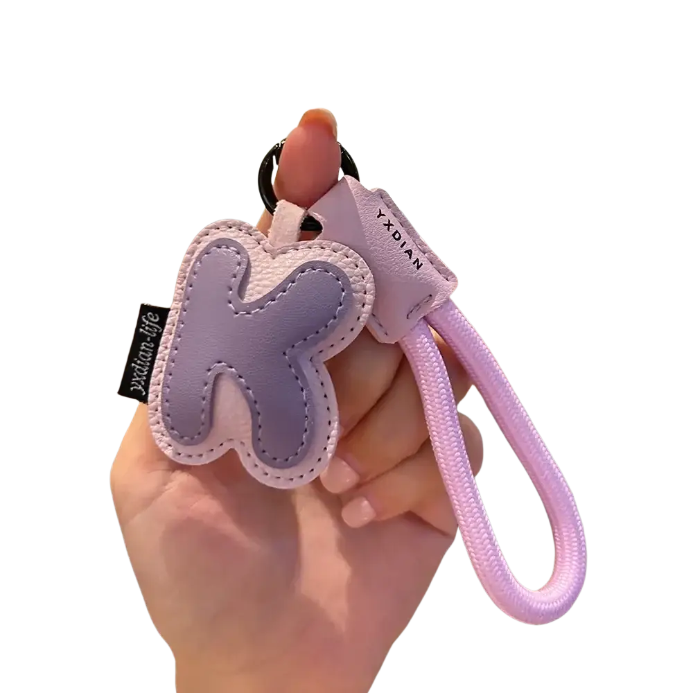 A soft lavender and pale pink leather initial keychain with stitched letter k and matching woven strap wristband charm