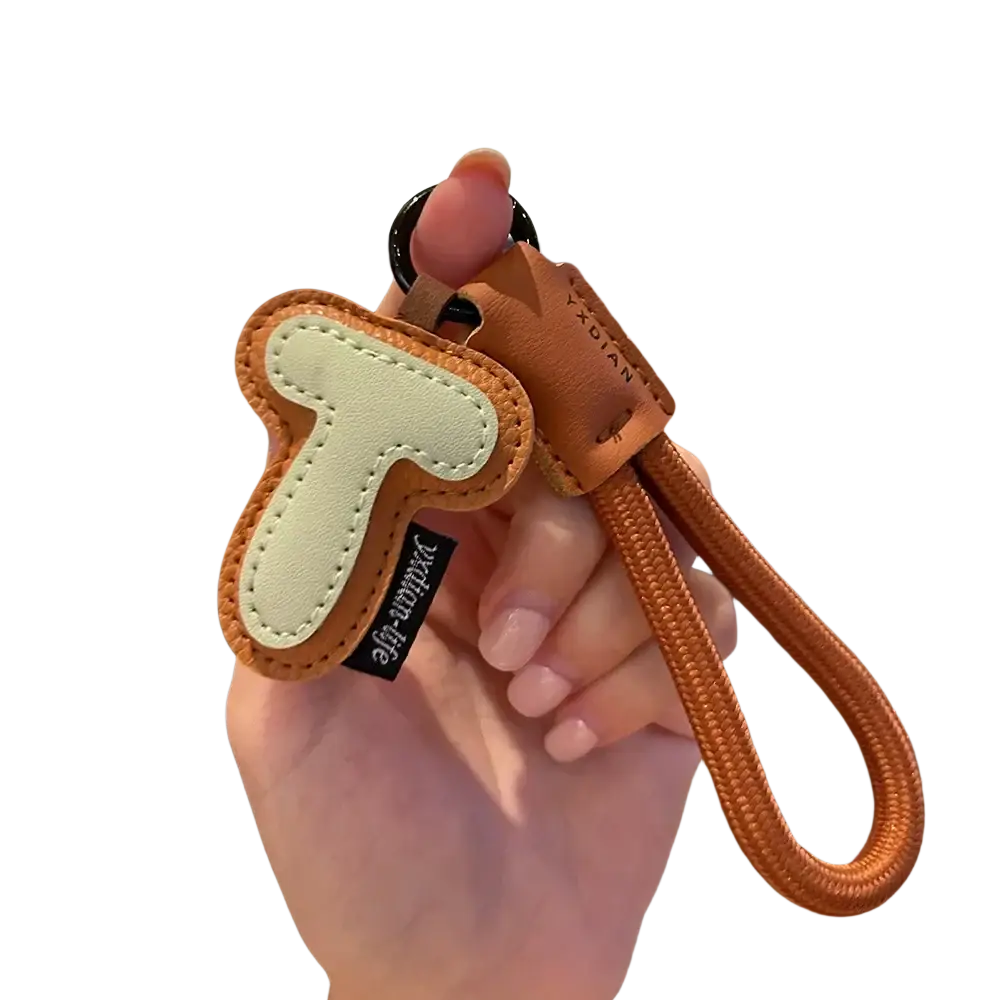 A tan leather initial keychain letter wristband charm with cream stitched t, black paddling life tag, and orange strap