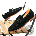 Black leather loafers with perforated suede texture, stitched detailing, and metallic buckle strap slip on shoes