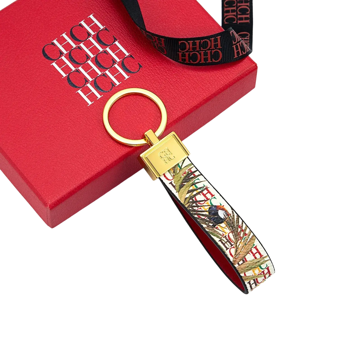 Leather logo keychain with gold-toned hardware, printed tropical bird and leaf fabric strap, and branded gold plaque