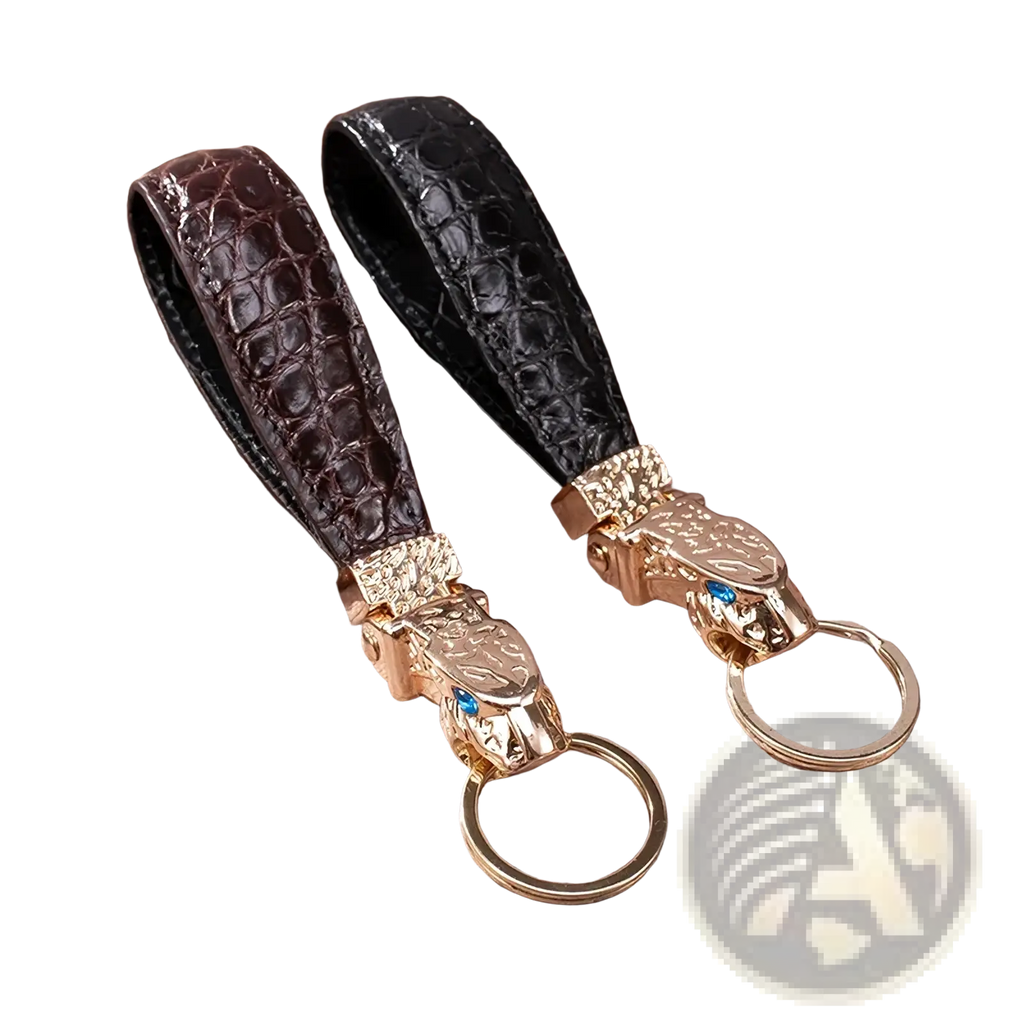 Two crocodile-patterned leather keychains in dark brown and black with gold tiger heads and blue gemstone eyes