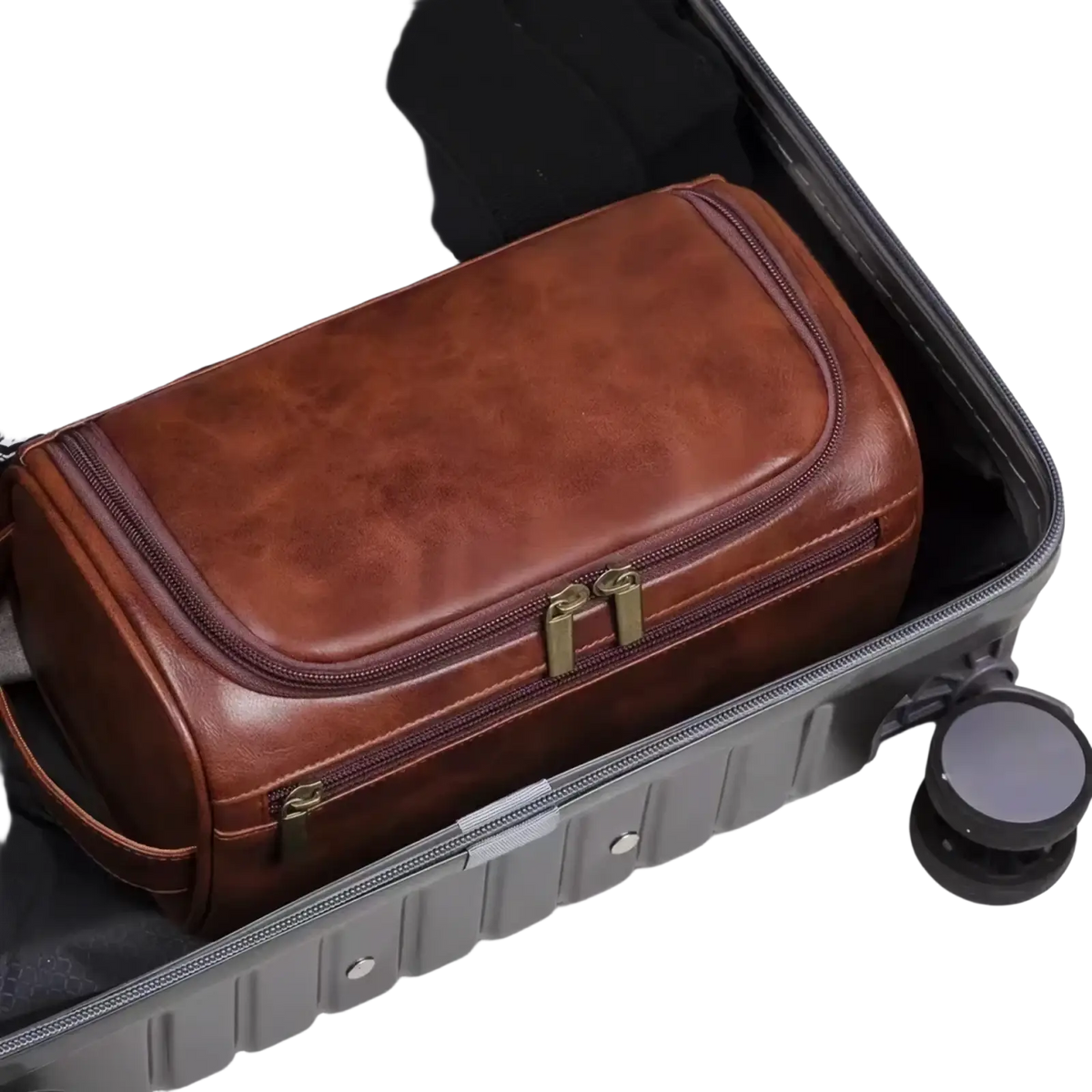 Brown leather toiletry bag with brass-colored zippers and handle inside an open suitcase for travel dopp kit use