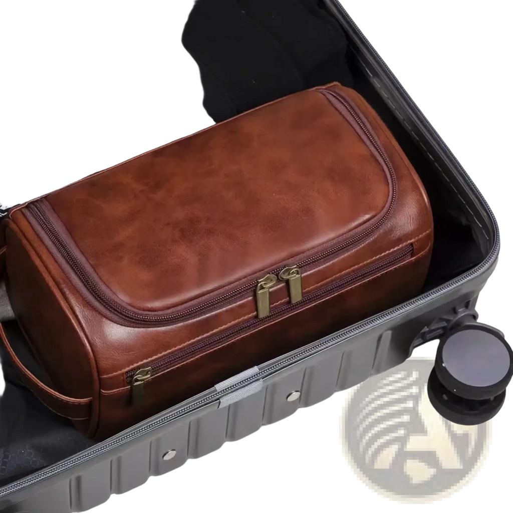 Brown leather toiletry bag with brass-colored zippers and handle inside an open suitcase for travel dopp kit use