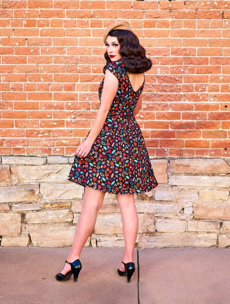 A woman wears a dark sleeveless vintage cotton a-line dress with vibrant red blue and yellow floral pattern
