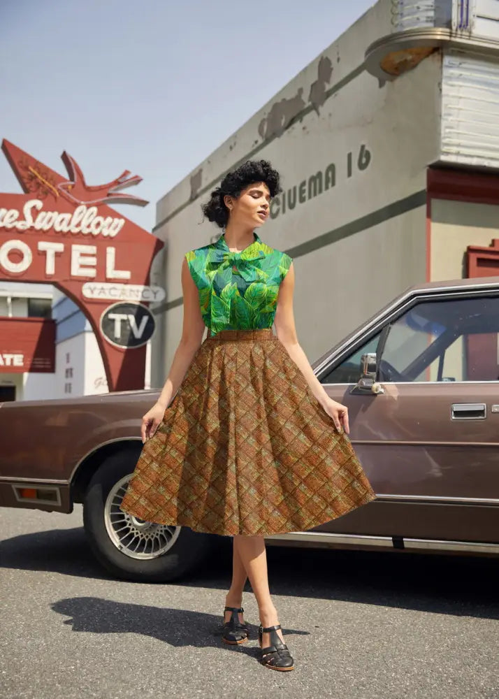 Woman wearing a green and brown tropical leaf print 1950s vintage cotton blouse with bow neckline
