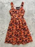 A sleeveless cotton fit and flare dress with a vibrant autumn oak leaves pattern in shades of orange red and brown