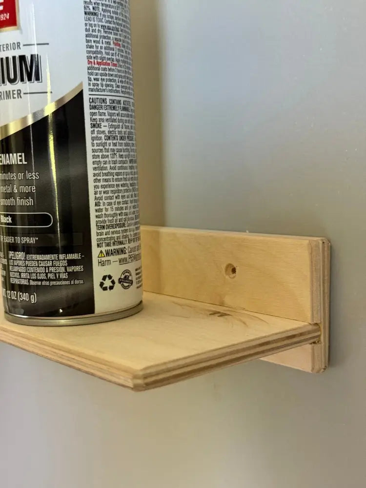 A can of black exterior enamel primer with white and gold label beside a light wood shelf of a white metal 36 inch garage ledge shelf and organizer bracket