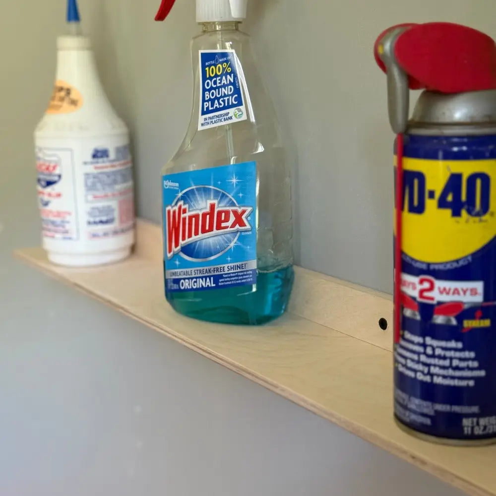 Clear plastic spray bottle with blue windex original liquid and white nozzle on white metal 36 inch garage ledge shelf organizer bracket