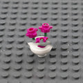 A white lego flower vase with two vibrant pink plastic flowers and green stems from lego flower vase set for kids