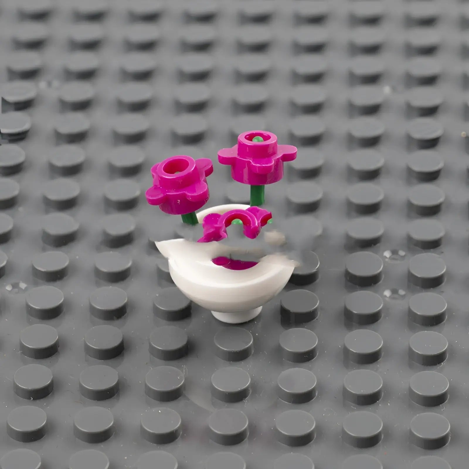 A white lego flower vase with two vibrant pink plastic flowers and green stems from lego flower vase set for kids
