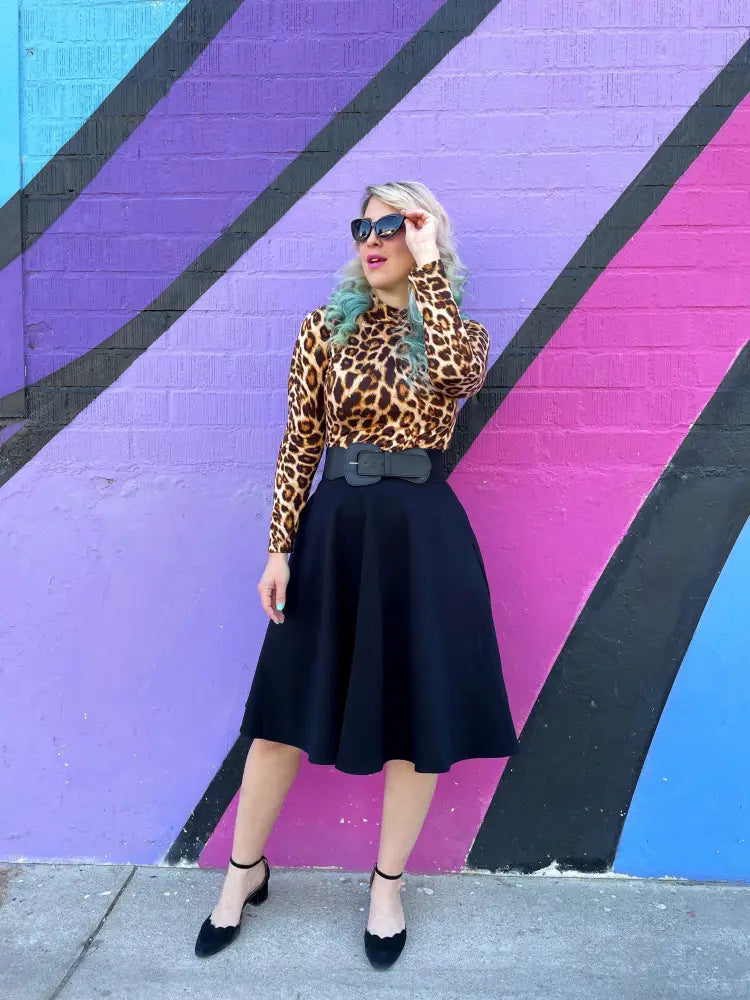 A woman wearing a vintage leopard print mock neck long sleeve top paired with a black skirt and wide belt