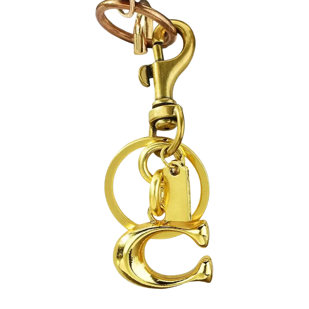 Gold-colored metal keychain with c initial charm and circular ring attached to white quilted leather bag