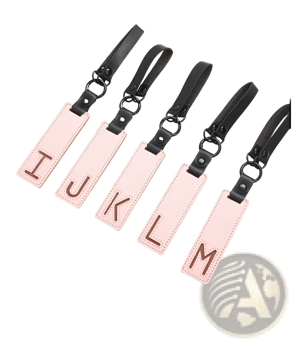 Pink leather luggage tags with black straps and metal rings featuring brown embossed uppercase letters for alphabet keychains