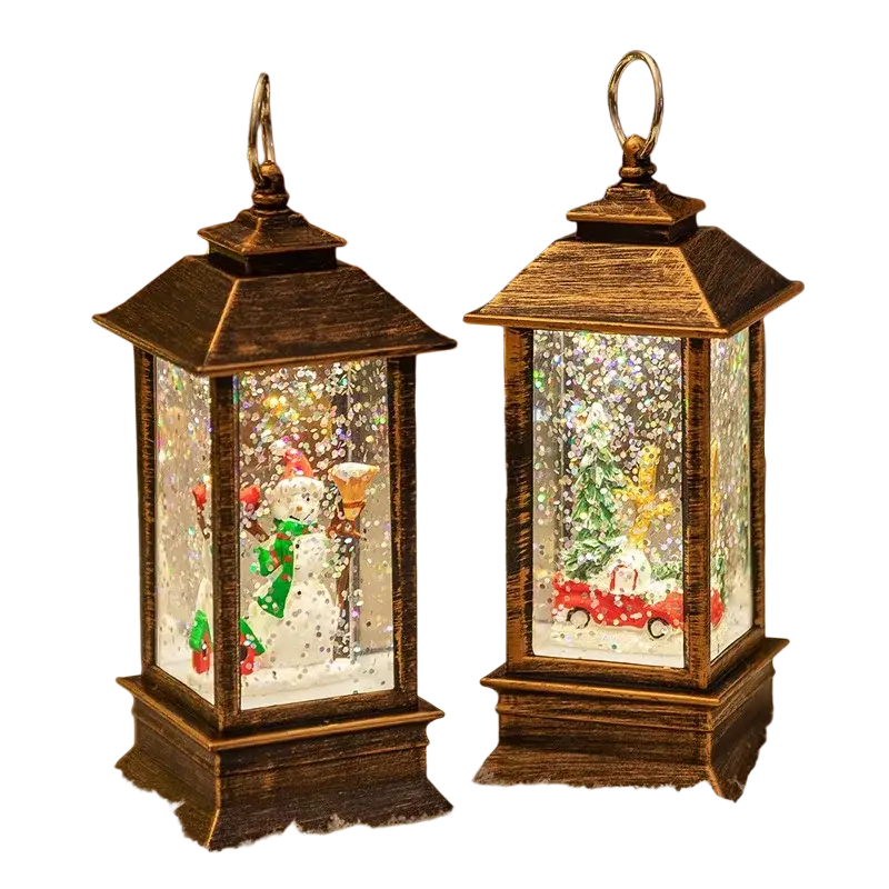 Two lighted bronze christmas snow globe lanterns with metal frames and illuminated winter scenes inside clear glass panels