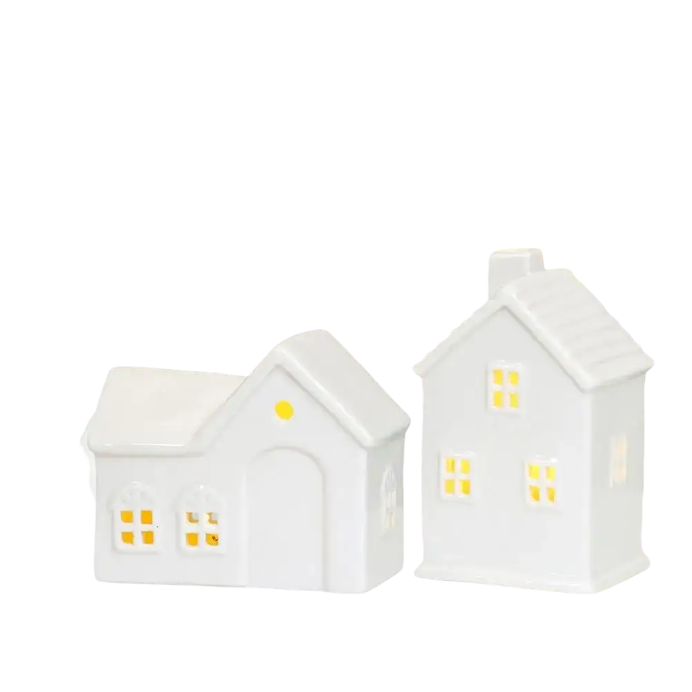 White ceramic christmas village houses lanterns with glowing windows and a green plant sprig for enchanting winter wonderland decor