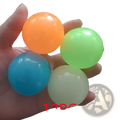 A hand holds four colorful translucent luminous sticky wall balls glow in the dark squeeze toys in orange green blue and white