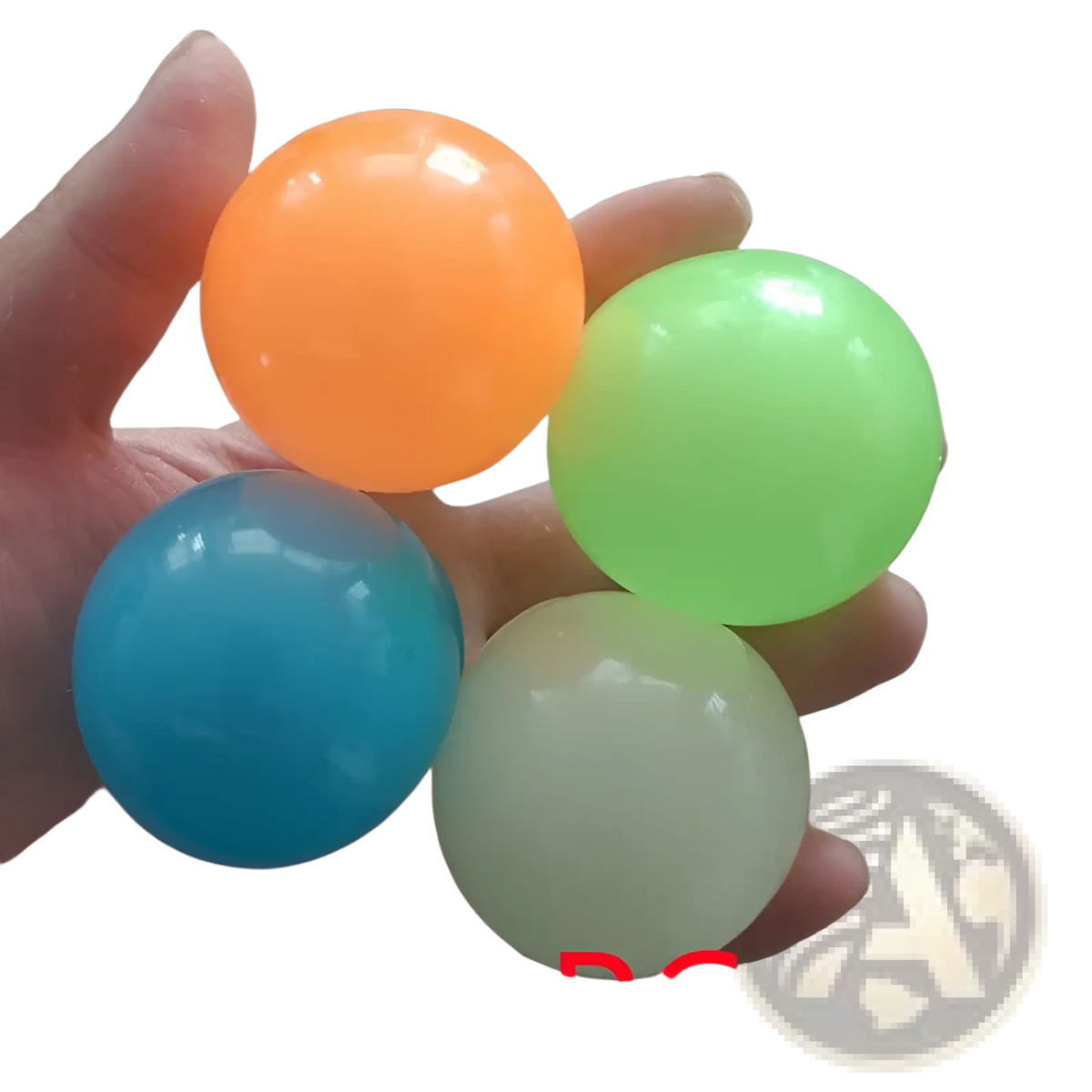 A hand holds four translucent glossy plastic luminous sticky wall balls in orange green blue and pale yellow glow in the dark