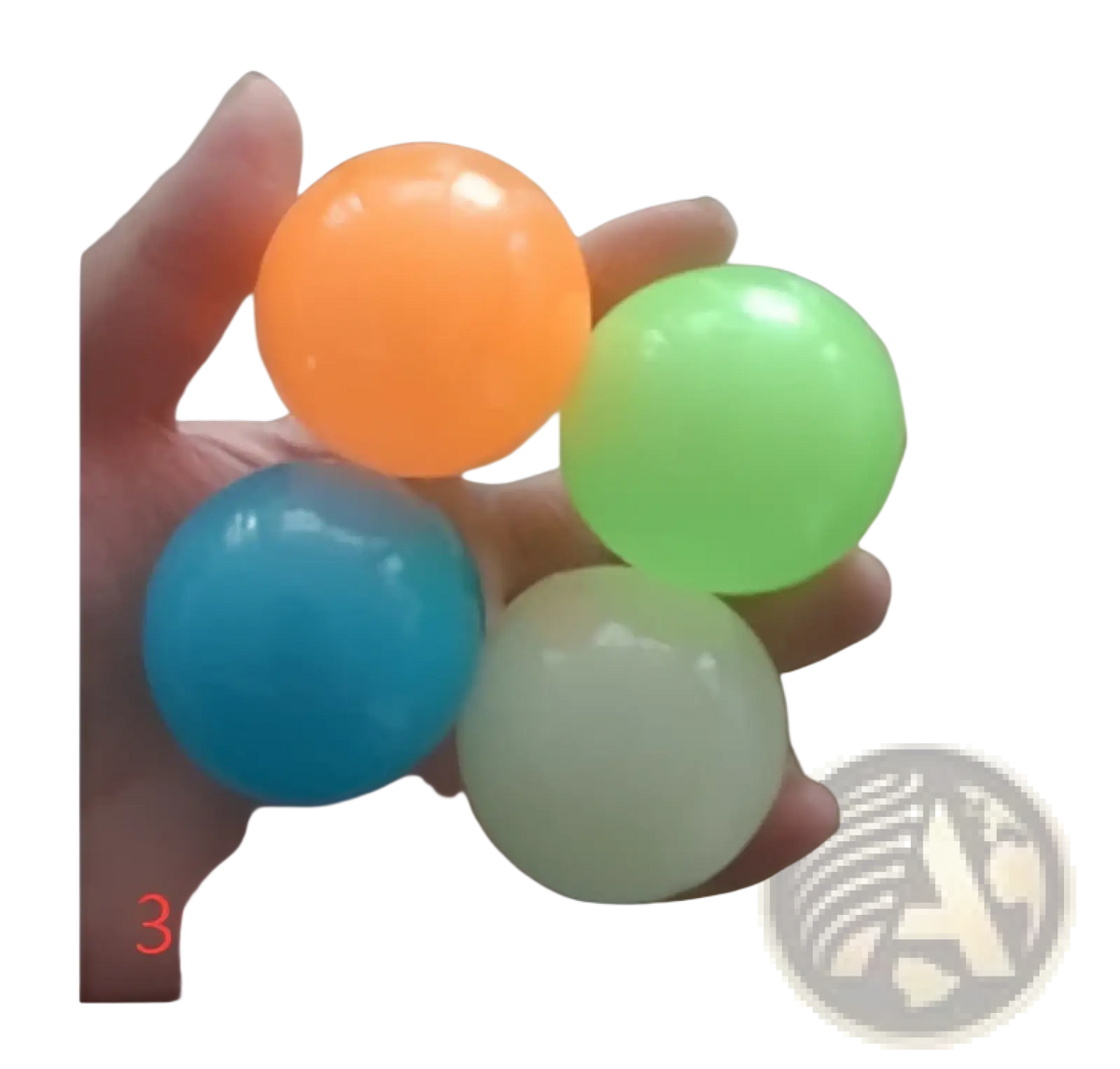 A hand holds four translucent glossy luminous sticky wall balls glow in the dark squeeze toy in orange green blue and white