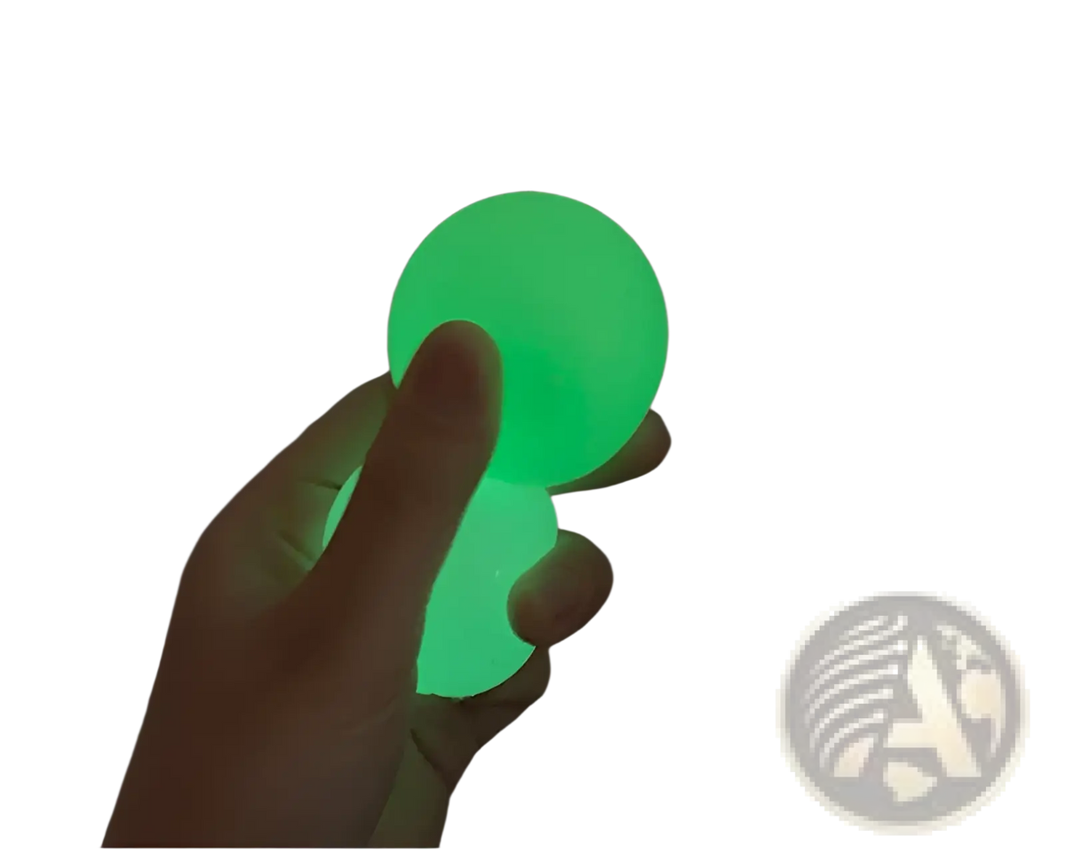 A glowing green luminous sticky wall ball made of smooth silicone held in a hand as a glow in the dark squeeze toy