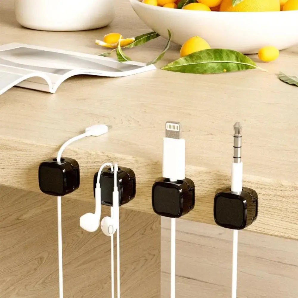 Black magnetic square under desk cable organizers holding white charging cables and earphones for cord management