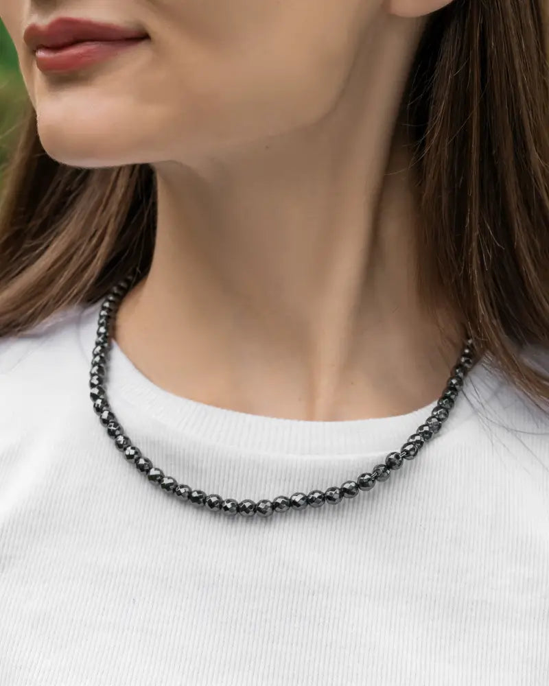 A sleek black faceted magnetic hematite 6mm beaded necklace with smooth rounded texture worn around the neck