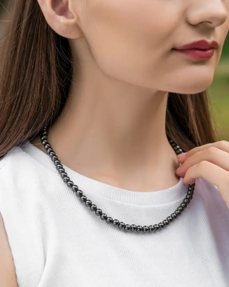 A sleek dark gray polished 6mm magnetic hematite round bead necklace worn around the neck