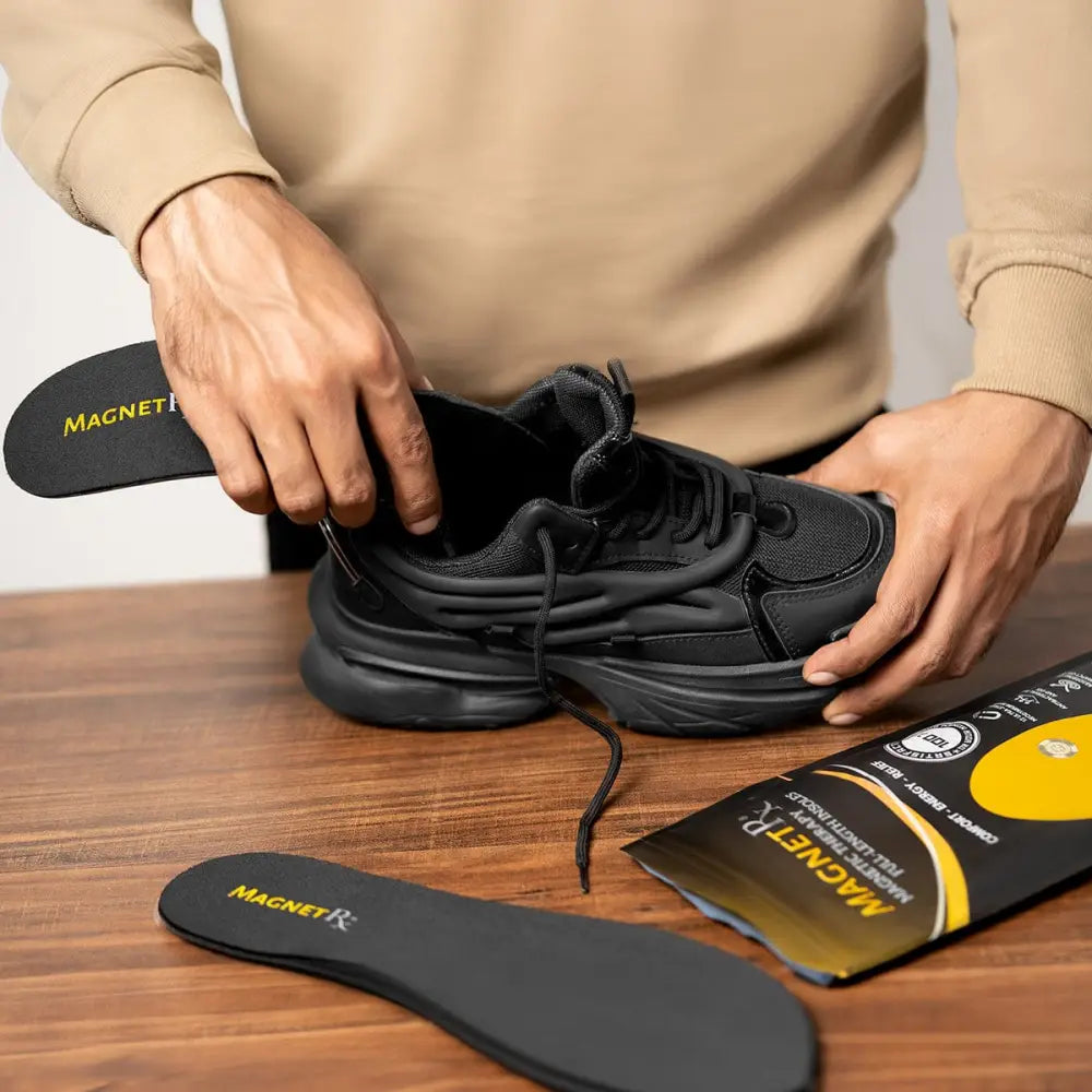 Black magnetic neodymium high power therapy insole with yellow branding being inserted into black sneaker
