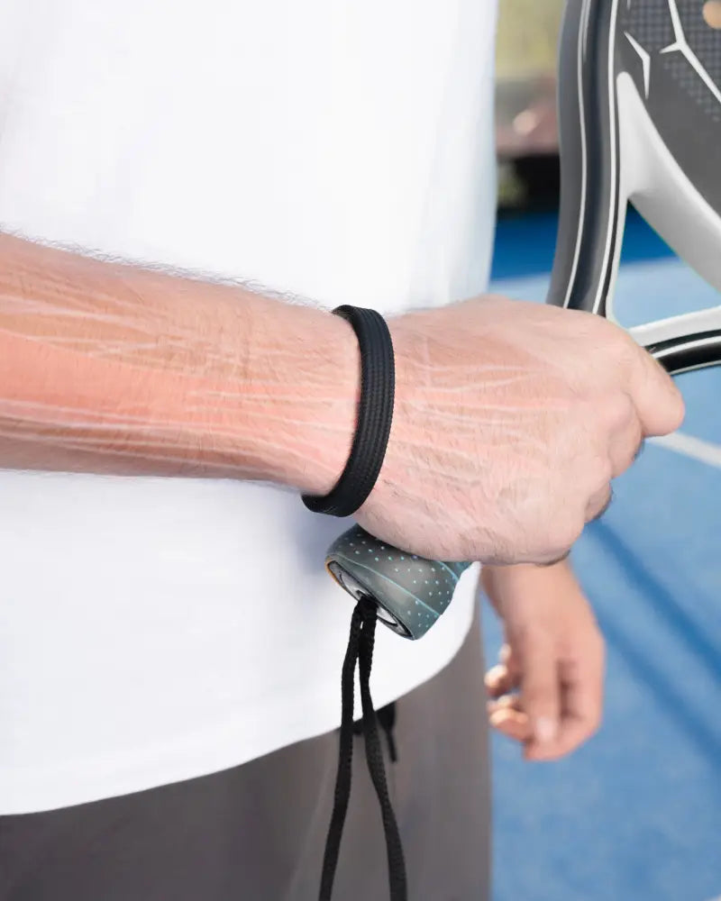 Black elastic magnetic silicone wristband worn on arm while holding tennis racket in Magnetrx Classic bracelet product image