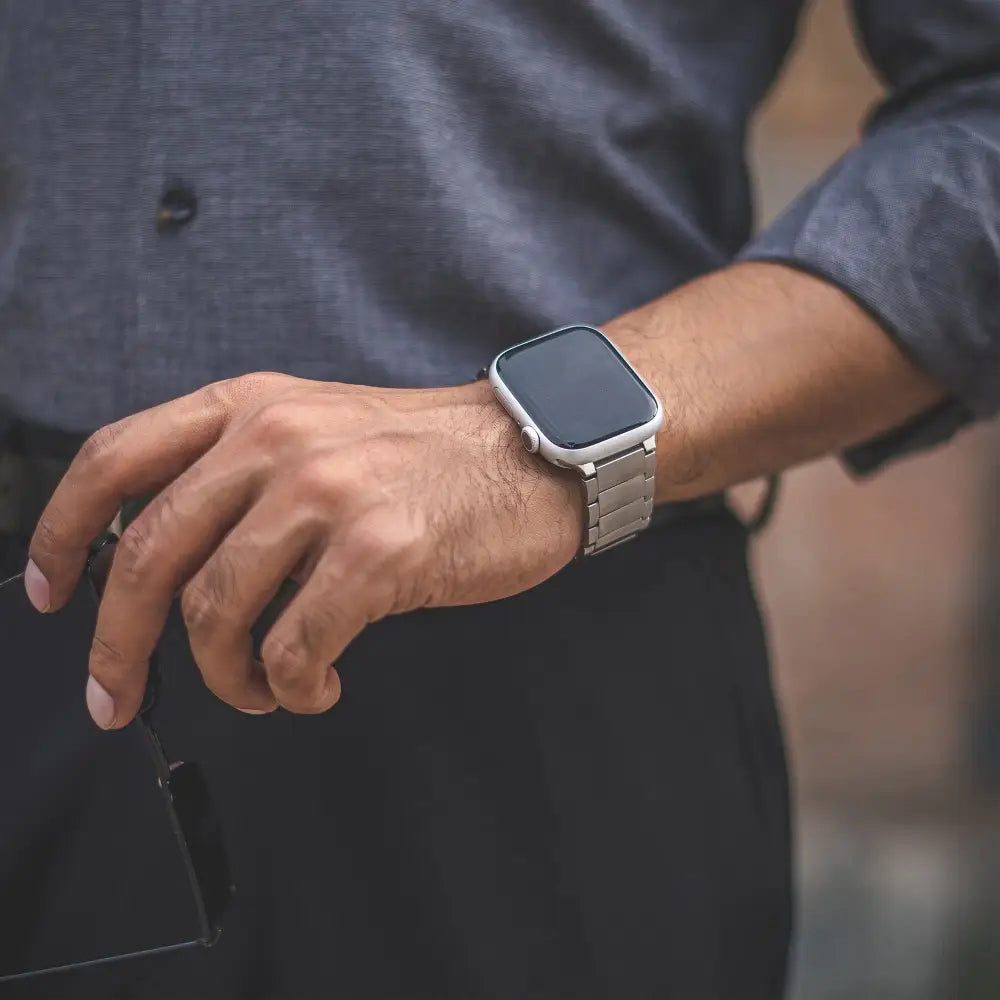 A sleek silver stainless steel magnetic therapy apple watch band with a square face worn on a wrist