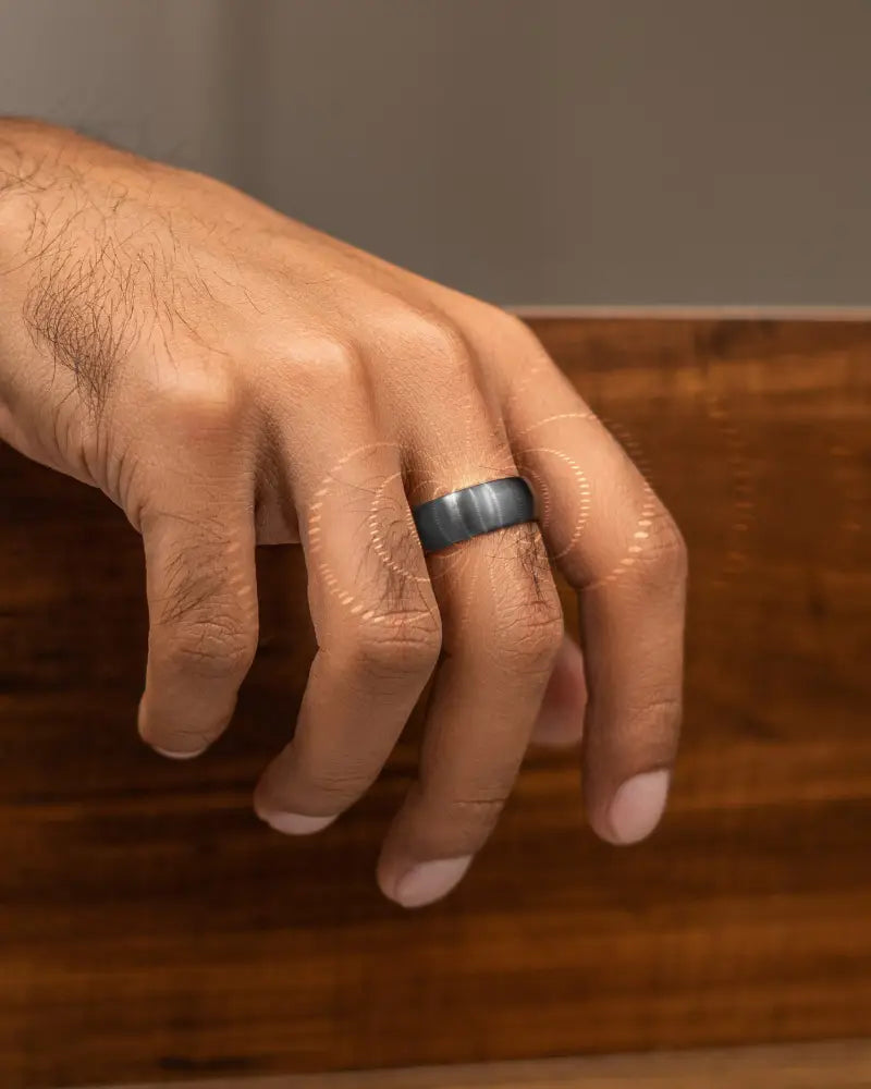 A sleek dark gray titanium gunmetal matte magnetic neodymium therapy ring with a smooth modern design worn on a finger