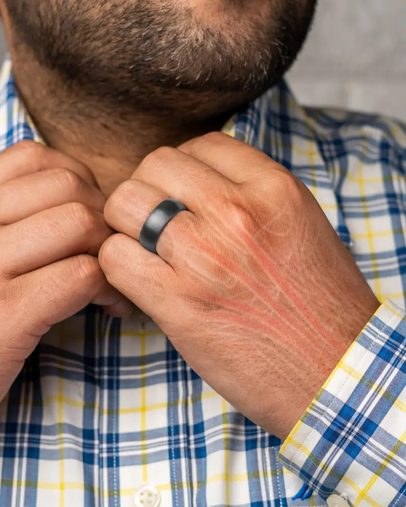 A sleek matte black gunmetal neodymium therapy ring with a smooth modern design worn on a mans finger