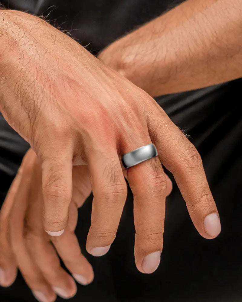 A sleek polished silver neodymium magnetic therapy wedding band with a smooth curved profile on a man’s ring finger