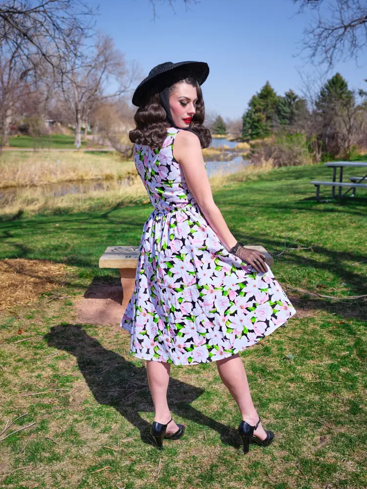 A woman wears a sleeveless magnolia floral cotton 1950s style midi dress with pockets in light lavender