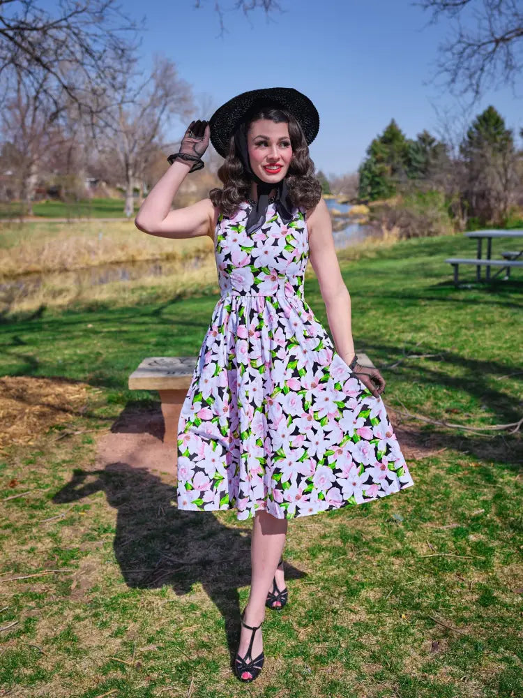 A sleeveless black cotton midi dress with vibrant pink floral pattern green leaves and pockets in 1950s style