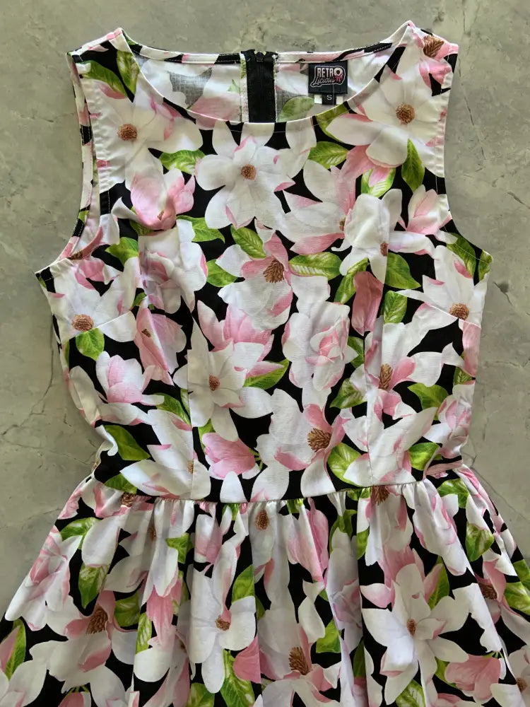 A sleeveless black cotton midi dress with vibrant white and pink magnolia floral pattern and retro 1950s style pockets